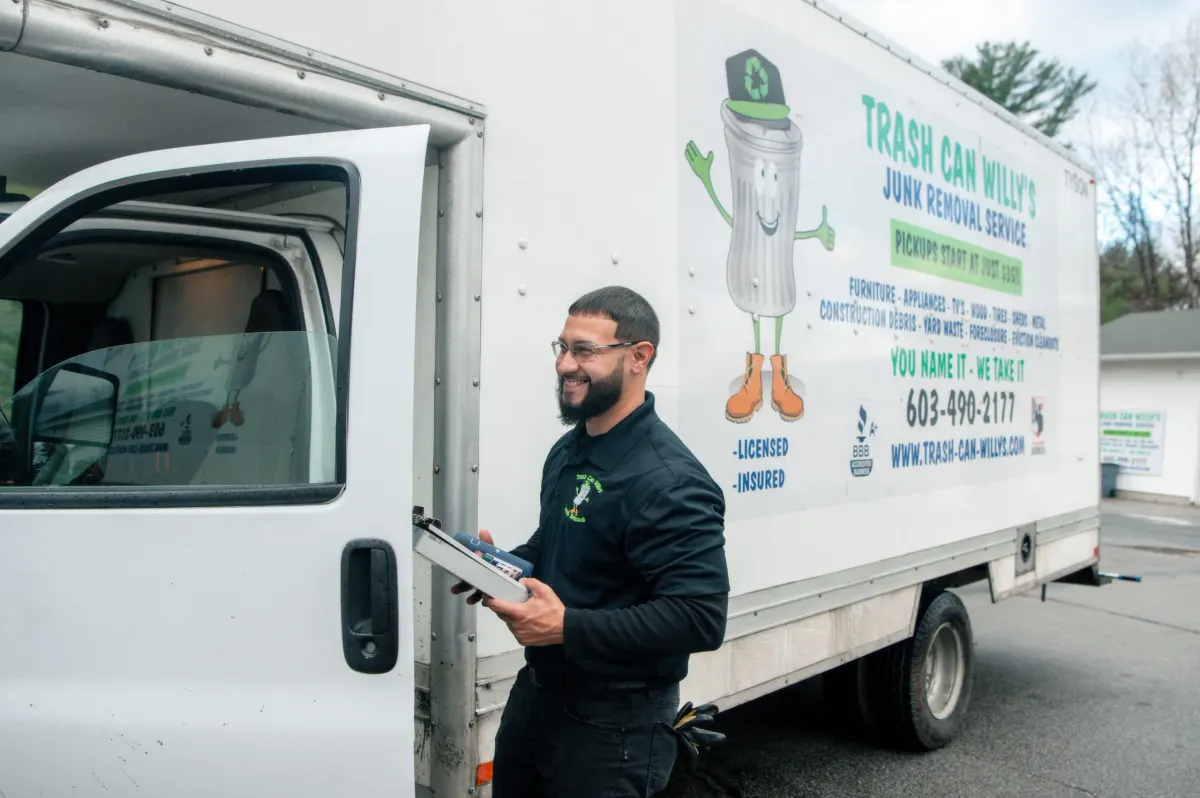 A crew member with a clipboard beside a Trash Can Willy's box truck