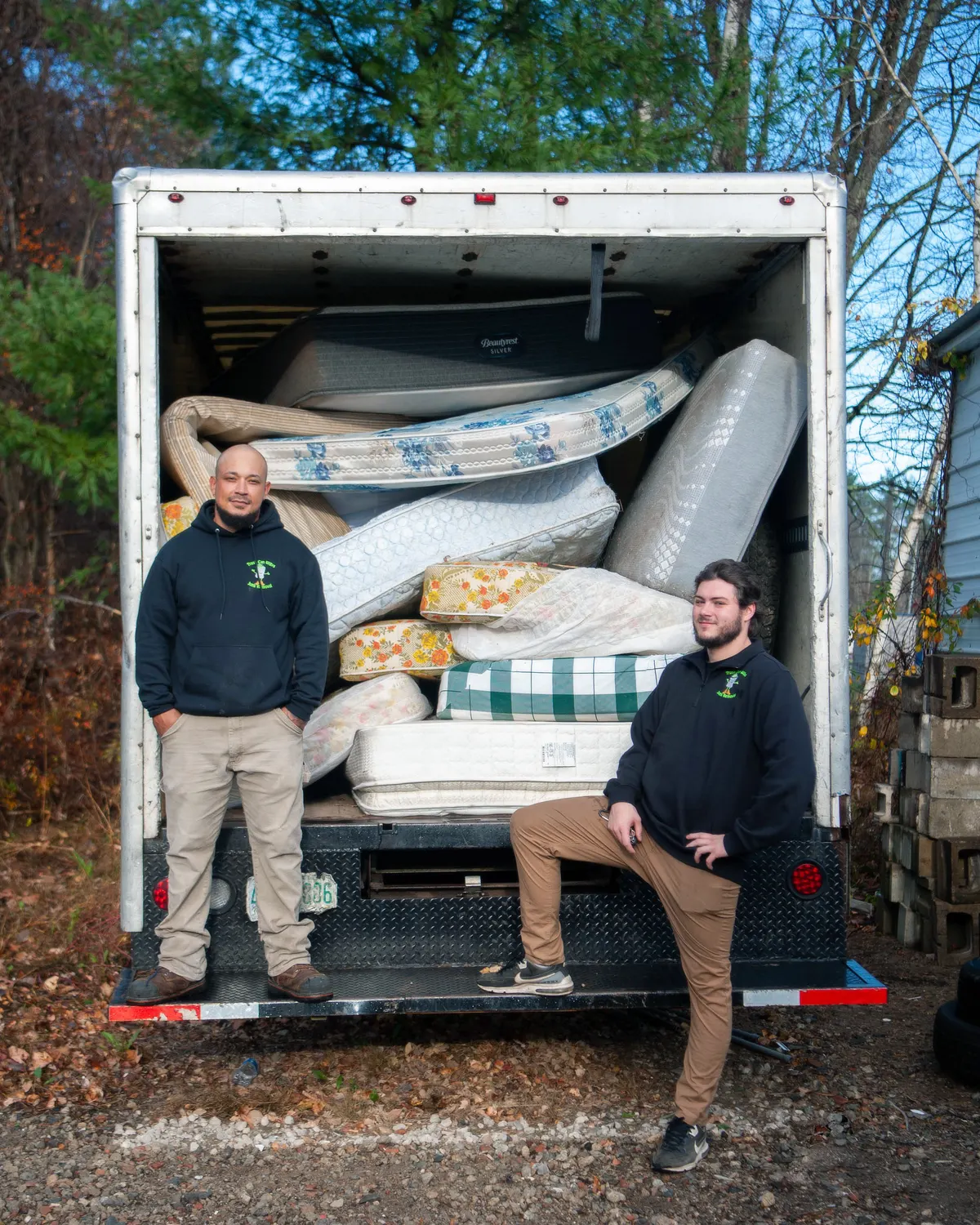 Two crew members at the open back of a Trash Can Willy's box truck loaded with mattresses