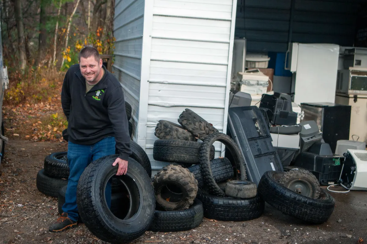 Old air conditioners, a freezer and other appliances stacked for recycling behind a load of tires