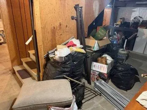 Bagged material and furniture piled at the foot of a basement staircase