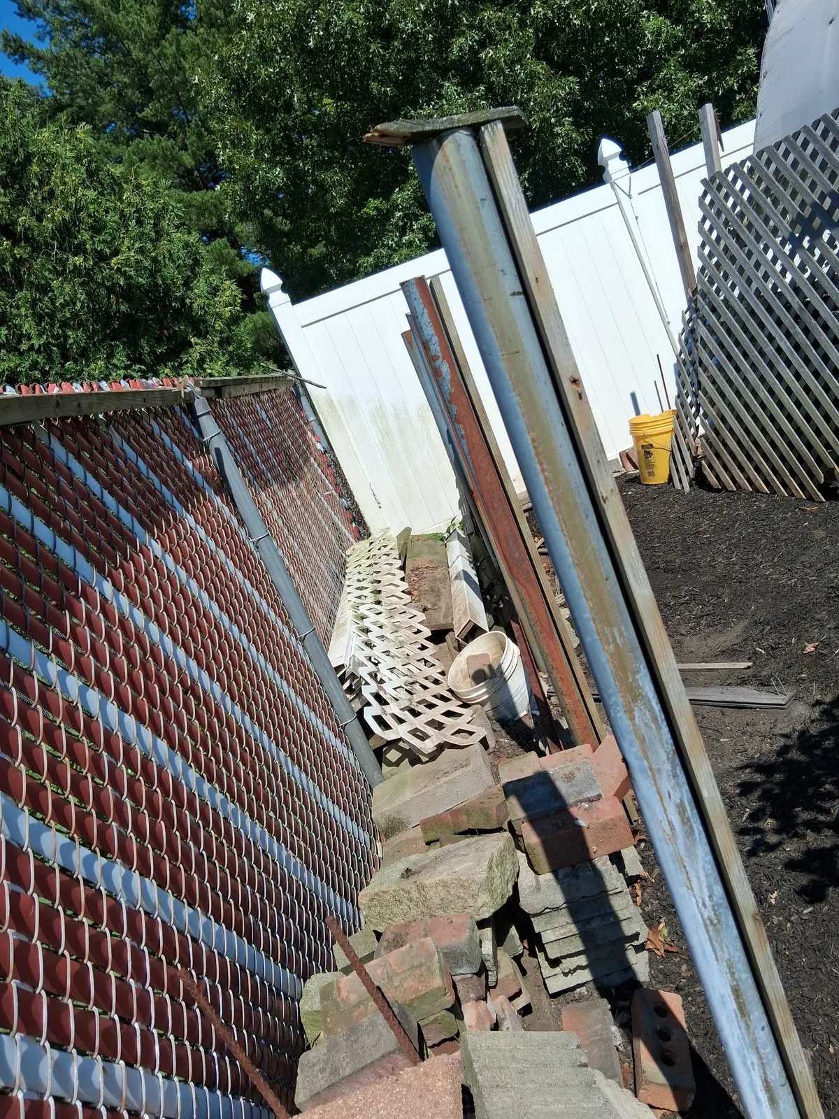 Pulled metal fence posts and rails stacked beside the old chain link run