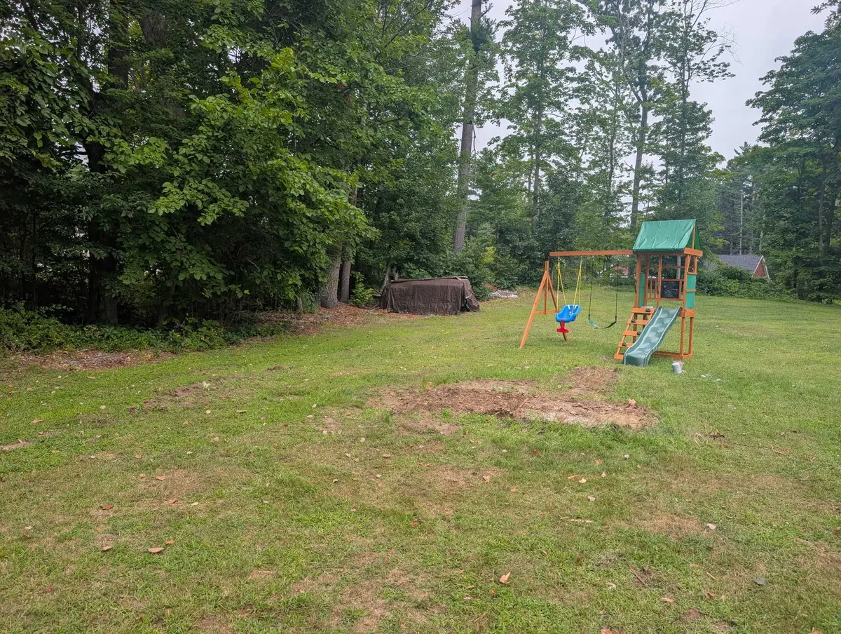 The same back yard after the playset came out, with a bare patch of ground where it stood and a smaller swing set still standing beside it