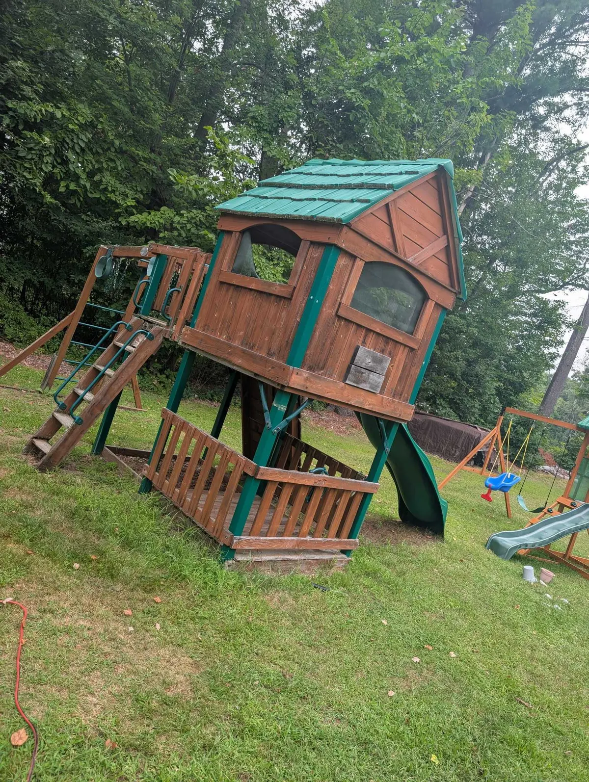 A wooden playset with a slide and swings before takedown