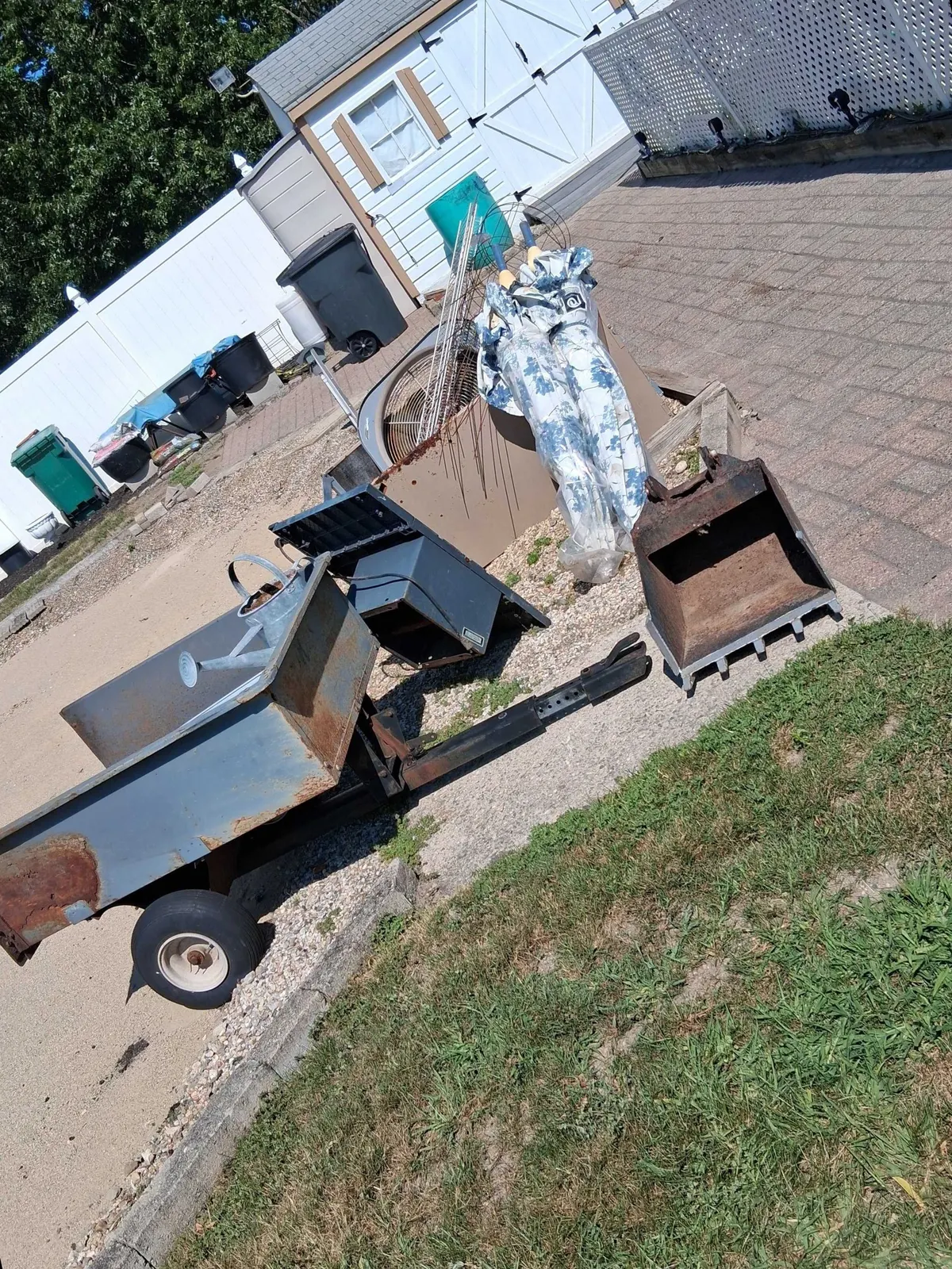 An old utility trailer loaded with scrap metal on a driveway, waiting to be hauled