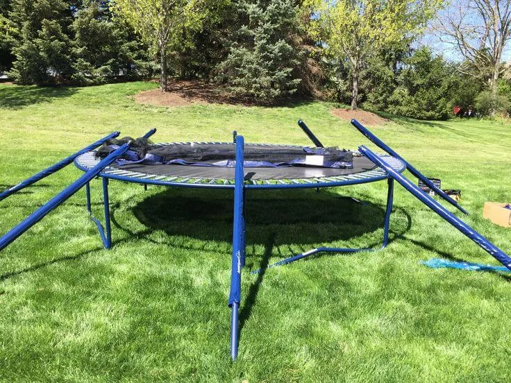 A backyard trampoline mid-teardown, its legs and enclosure poles unbolted and laid across the mat