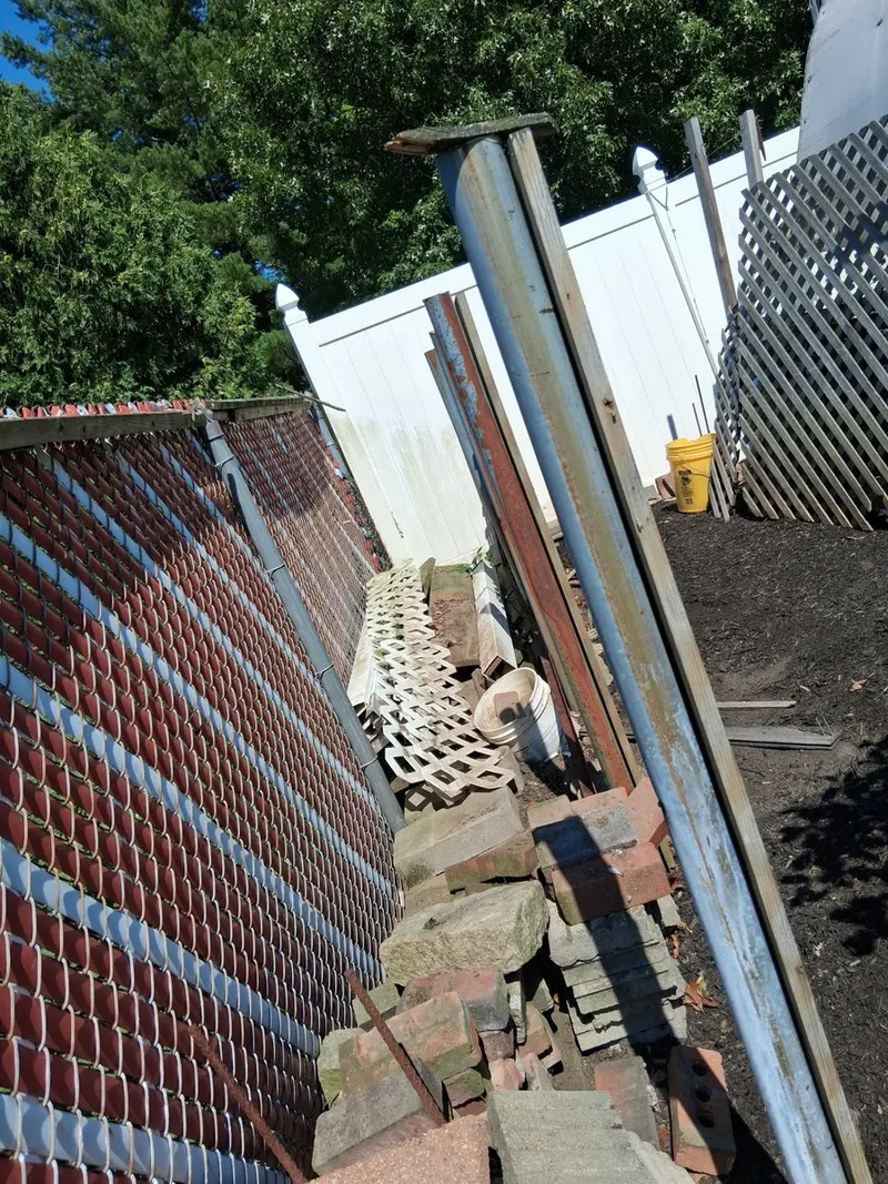 An old chain link fence with privacy slats, its metal posts and rails pulled out and stacked alongside